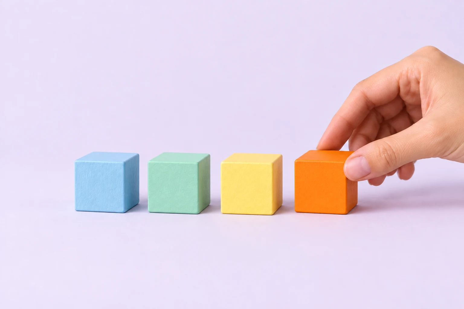 Une main pose un cube orange au bout d’une rangée de cubes en bois pastel